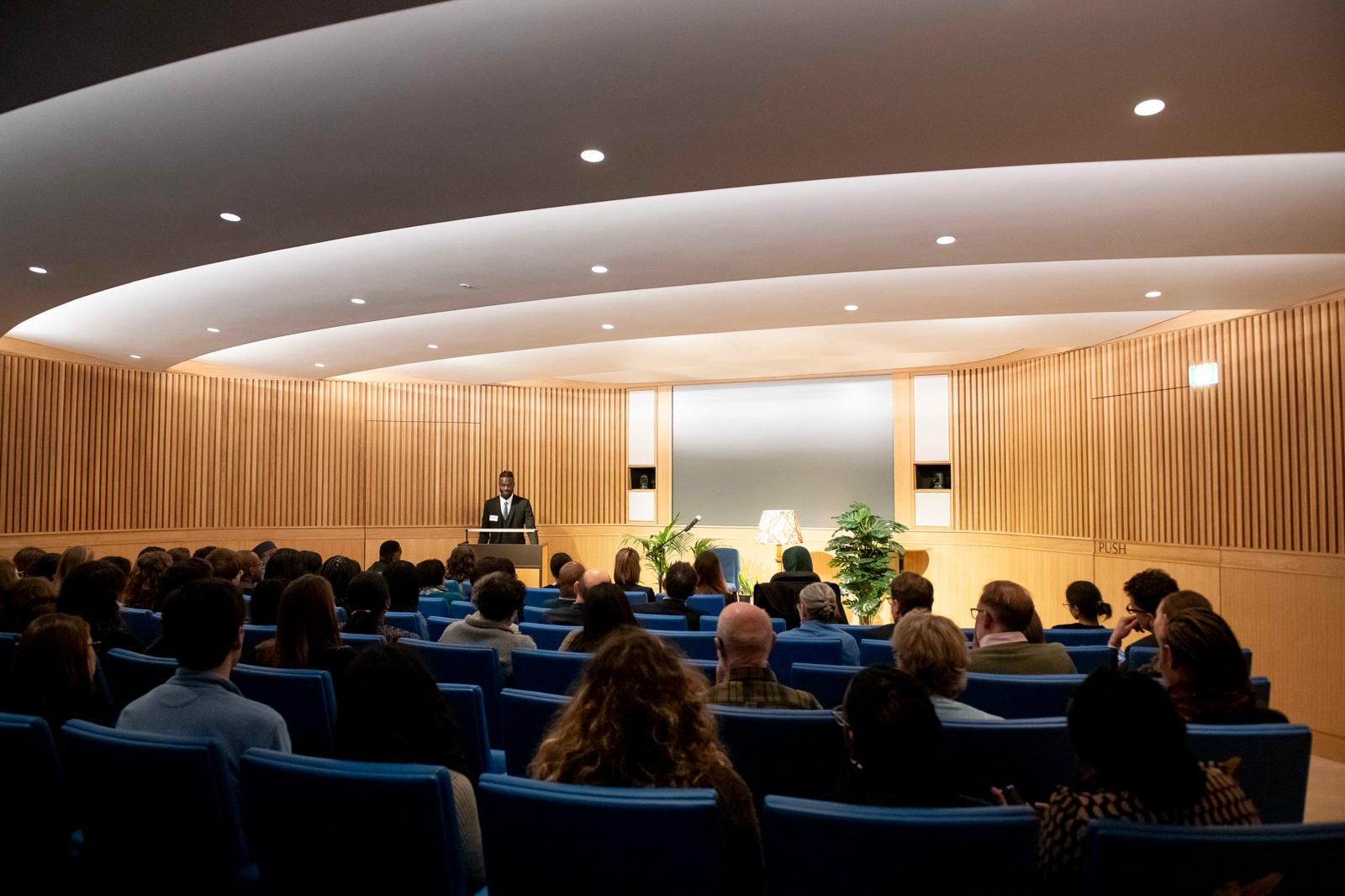 Mass Ndow-Njie addressing a full auditorium
